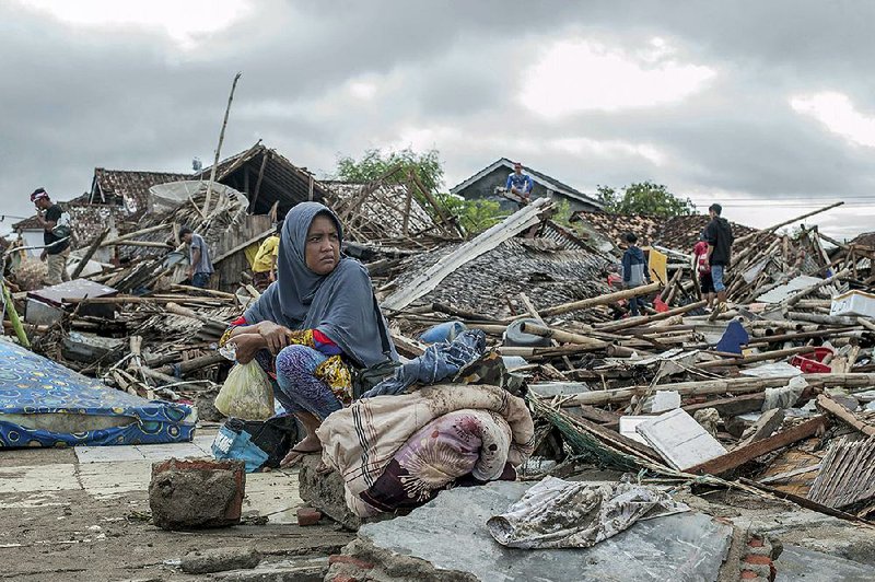 A tsunami survivor sits among the debris Monday as she salvages items from where her home used to stand in Sumur, Indonesia. 
