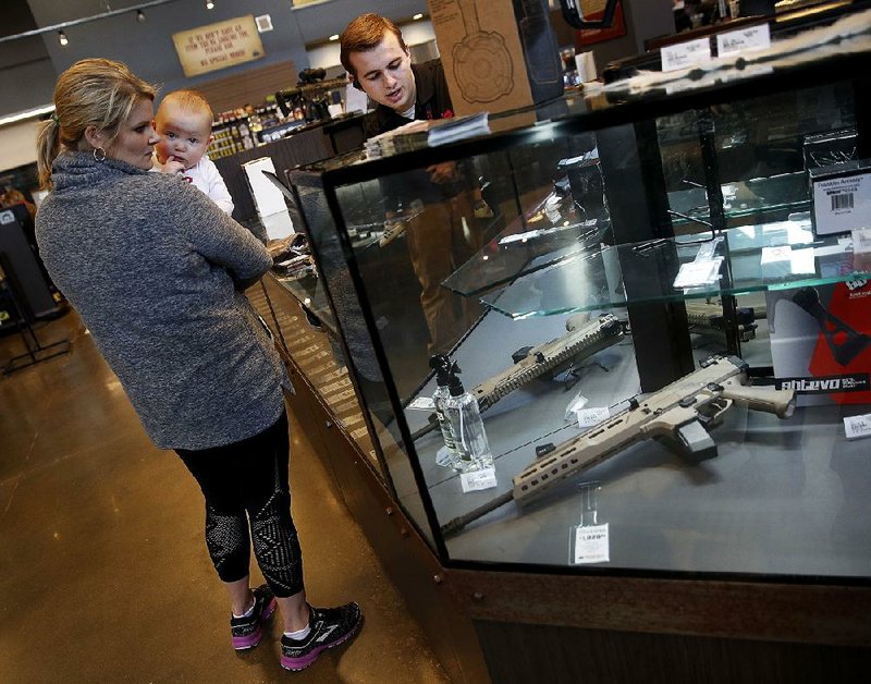 A salesman points out features on a handgun for Anne Vifquain while she holds her son Gavin at the Frontier Justice store in Lee’s Summit, Mo., earlier this month. 