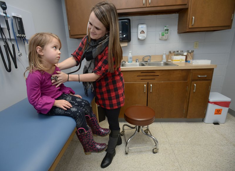 NWA Democrat-Gazette/ANDY SHUPE Tera Thompson, an advanced practice registered nurse with Washington Regional, uses a stethoscope Dec. 18 while demonstrating the use of one of the Lincoln School-Based Health Center's examination rooms by checking out her daughter, Layla Thompson, 4, who was feeling ill.