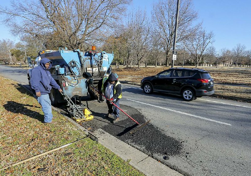 Danny Jackson (left) and Peter Owens, with the Little Rock Public Works Department, fill in a pothole Friday morning on Riverfront Drive.
