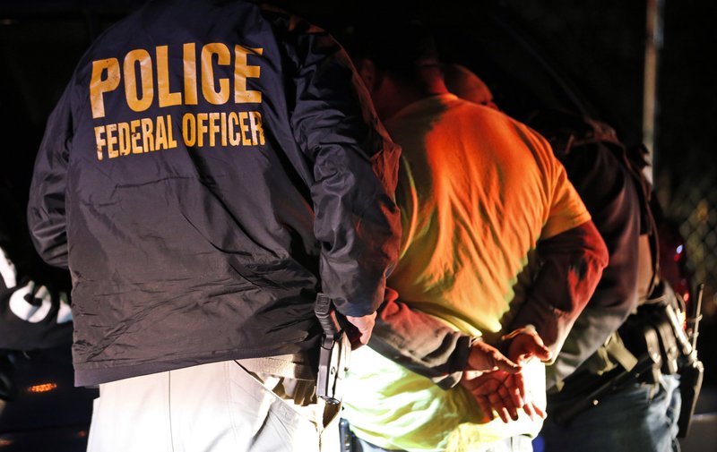In this Oct. 22, 2018, photo U.S. Immigration and Customs Enforcement agents surround and detain a person during a raid in Richmond, Va. ICE's enforcement and removal operations, like the five-person field office team outside Richmond, hunt people in the U.S. illegally, some of whom have been here for decades, working and raising families. Carrying out President Donald Trump's hard-line immigration policies has exposed ICE to unprecedented public scrutiny and criticism, even though officers say they're doing largely the same job they did before the election, prioritizing criminals. (AP Photo/Steve Helber)