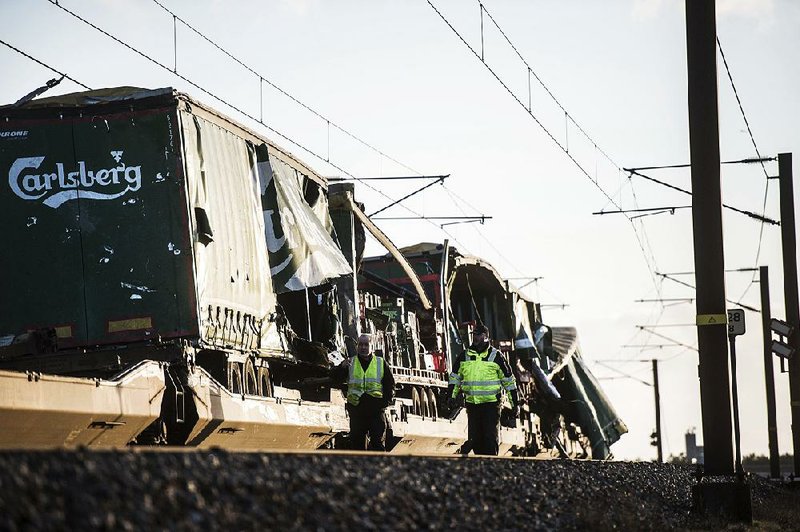 People walk near the damaged cargo compartments of a freight train parked Wednesday near a bridge outside Nyborg, Denmark. 