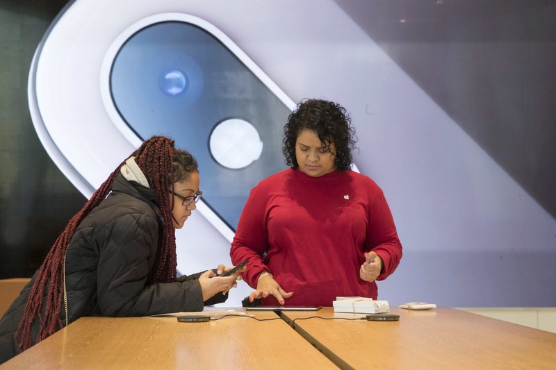 An image of an iPhone is on display in the background as a customer, left, is helped at the Apple store in the Brooklyn borough of New York, Thursday, Jan. 3, 2019. Apple's shock warning that its Chinese sales are weakening ratcheted up concerns about the world's second largest economy and weighed heavily on global stock markets as well as the dollar on Thursday. (AP Photo/Mary Altaffer)