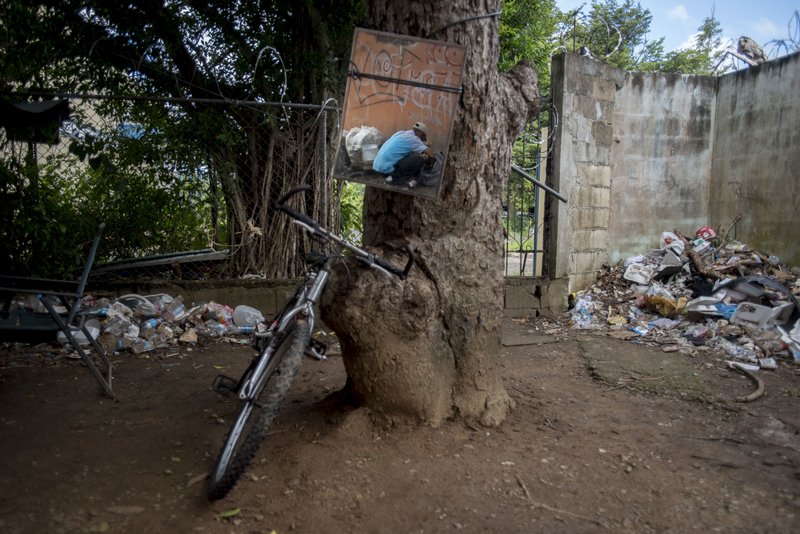 In this Dec. 14, 2018 photo, a mirror tied to a tree reflects a heroin addict preparing his dose, in an area popular with users behind an abandoned home in Humacao, Puerto Rico. Heroin addicts use the mirror to get a better view of themselves when injecting, especially when into their necks. (AP Photo/Carlos Giusti)