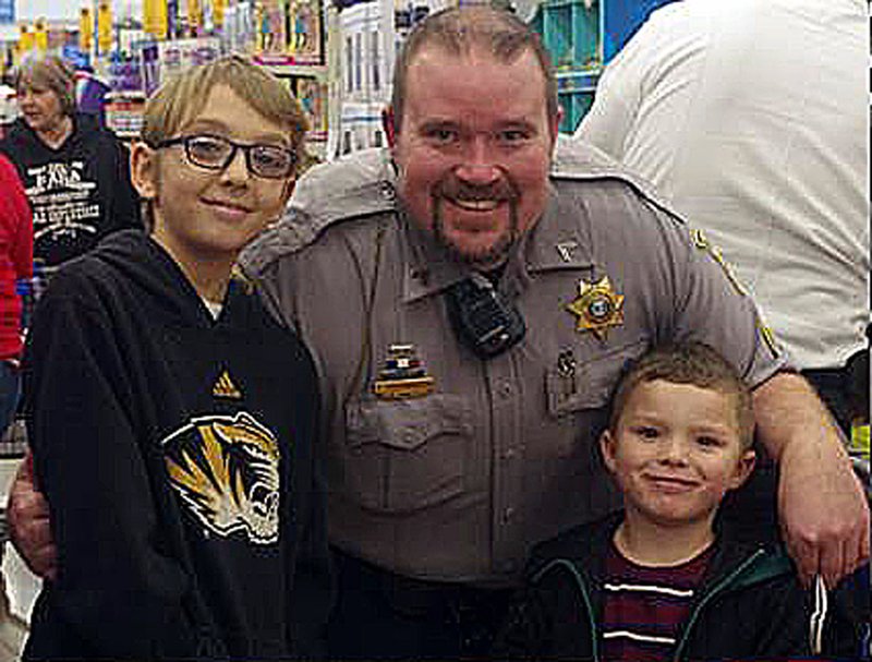 COURTESY PHOTO/Deputy Kyle Hackworth takes a moment from the excitement of Shop With a Hero to offer a smiling portrait with two children selecting Christmas gifts.
