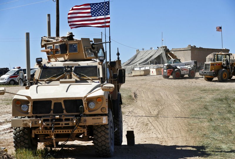 In this Wednesday, April 4, 2018 file photo, a U.S. soldier, left, sits on an armored vehicle behind a sand barrier at a newly installed position near the front line between the U.S-backed Syrian Manbij Military Council and the Turkish-backed fighters, in Manbij, north Syria. An American military official said Friday, Jan. 11, 2019 that the U.S.-led military coalition has begun the process of withdrawing troops from Syria. (AP Photo/Hussein Malla, File)