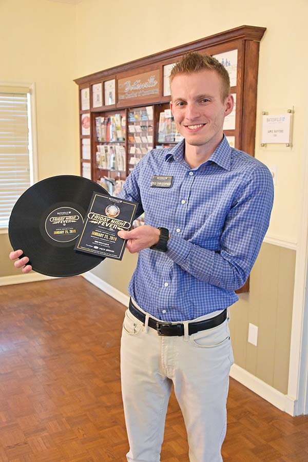 Kyle Christopher, tourism director for the Batesville Area Chamber of Commerce, holds a vinyl record and a flier for the annual chamber banquet, Friday Night Fever, set for Jan. 25 at the Batesville Community Center.