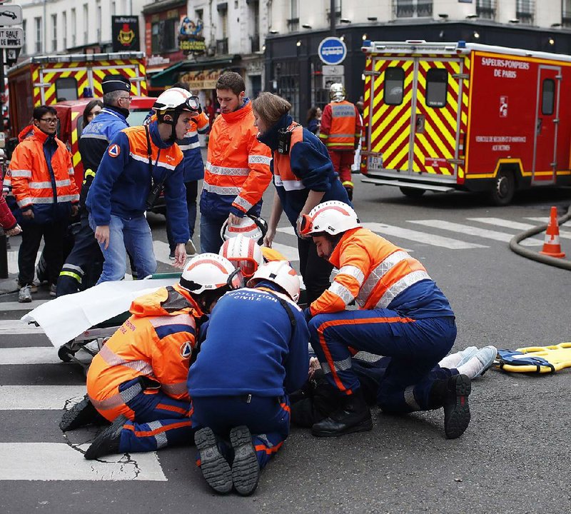 Firefighters treat an injured person Saturday after an explosion apparently caused by a gas leak blew apart a Paris bakery, killing three people and injuring dozens more. The blast shattered windows and overturned cars. 