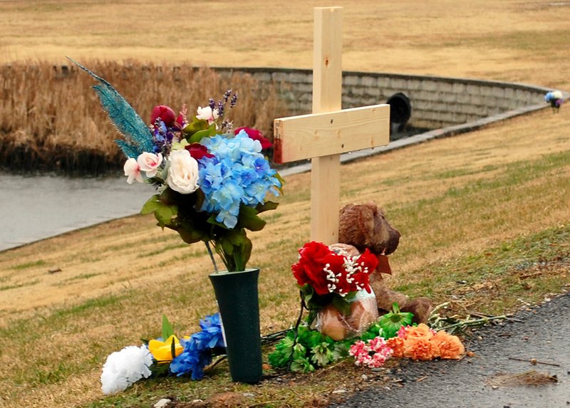 Hunter McFerrin/Siloam Sunday A cross, flowers, and a teddy bear rest near the pond located at the intersection of Main Street and U.S. Highway 412 on Friday morning, which is the location where Tyner Levi Hammett's accident took place.