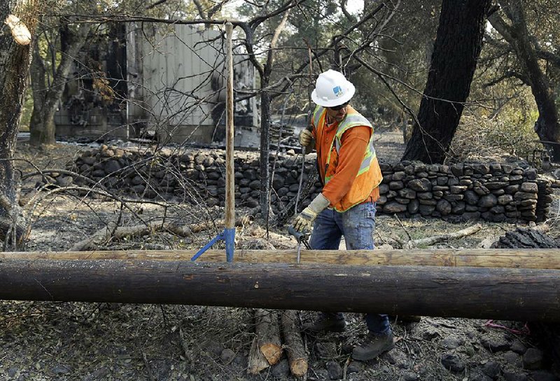 A Pacific Gas and Electric worker replaces power poles destroyed by an October wildfire in Glen Ellen, Calif. The potentially large liabilities over deadly California wildfires is forcing the utility to file for bankruptcy. 