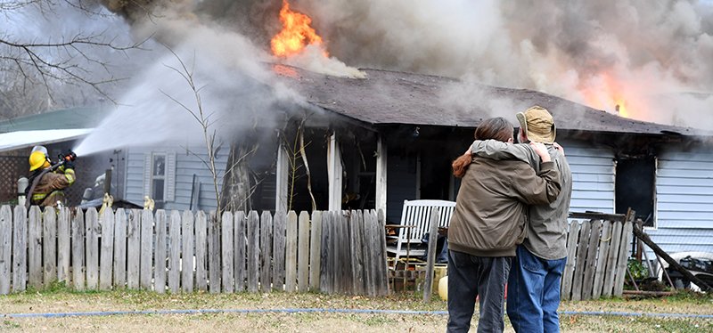 The Sentinel-Record/Grace Brown HOUSE FIRE: Residents of 302 Ninth St. in Mountain Pine watch as firefighters from the Mountain Pine and Piney fire departments work to control a fully involved house fire that occurred just before 3 p.m. Wednesday.