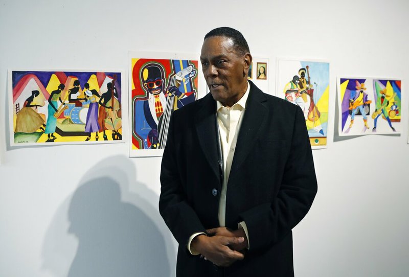 In this Thursday, Jan. 17, 2019 photo, Richard Phillips stands next to some of his artwork during an interview at the Community Art Gallery in Ferndale, Mich. Phillips was exonerated of murder in 2018 after 45 years in prison. Lawyers say he should be entitled to more than $2 million under Michigan's wrongful conviction law, but the state so far is resisting. So Phillips, 73, is selling some of his 400-plus watercolors that he painted in prison. (AP Photo/Carlos Osorio)