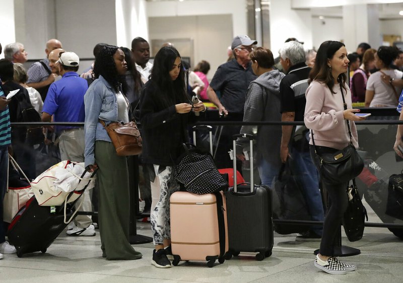 FILE- In this Jan. 18, 2019, file photo passengers wait in line at a security checkpoint at Miami International Airport in Miami. While security screeners and air traffic controllers have been told to keep working, Federal Aviation Administration safety inspectors weren't, until the agency began recalling some Jan. 12. About 2,200 of the more than 3,000 inspectors are now back on the job, overseeing work done by airlines, aircraft manufacturers and repair shops. The government says they're doing critical work but forgoing such tasks as issuing new pilot certificates.(AP Photo/Lynne Sladky, File)