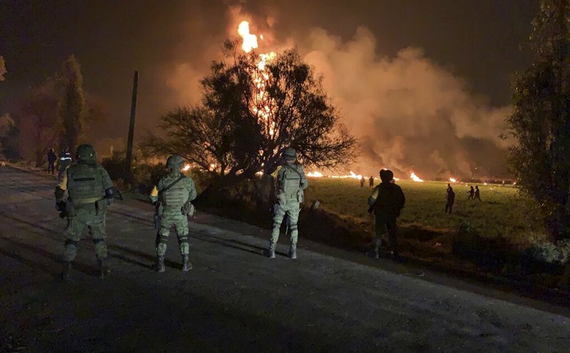 In this image provided by the Secretary of National Defense, soldiers guard the area by an oil pipeline explosion in Tlahuelilpan, Hidalgo state, Mexico, Friday, Jan. 18, 2019. A huge fire exploded at a pipeline leaking fuel in central Mexico on Friday, killing at least 21 people and badly burning 71 others as locals were collecting the spilling gasoline in buckets and garbage cans, officials said. Officials said the leak was caused by an illegal tap that fuel thieves had drilled into the pipeline in a small town in the state of Hidalgo, about 62 miles (100 kilometers) north of Mexico City. (Secretary of National Defense via AP)