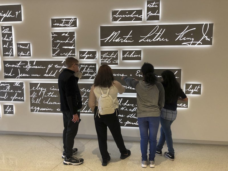 In this Friday, Jan. 18, 2019 photo, visitors look at a new metal sculpture at the National Center for Civil and Human Rights in Atlanta that features the words of the Rev. Martin Luther King Jr. in his own handwriting illuminated by light. The permanent sculpture hangs just outside a gallery where an exhibit of King's papers, including drafts of famous speeches and notable sermons, is on display. (AP Photo/Kate Brumback)