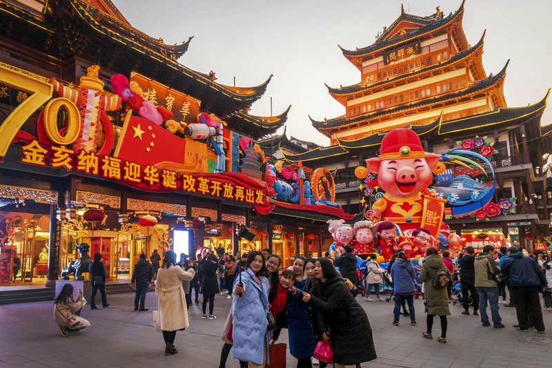 In this Jan. 17, 2019, photo, women take a selfie as others tour at the Yu Garden decorated with pig statues for Lunar New Year in Shanghai. China's 2018 economic growth fell to a three-decade low as activity cooled amid a tariff war with Washington. (Chinatopix via AP)