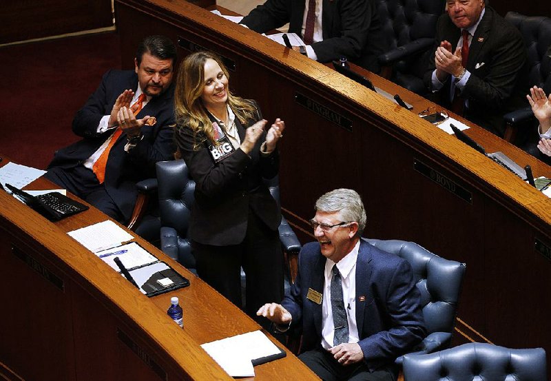 Sen. Jason Rapert (left) and Sen. Missy Irvin join in the Senate chamber in applauding Sen. Ricky Hill (bottom) during an exchange over a bill concerning the reorganization of municipal governments. 