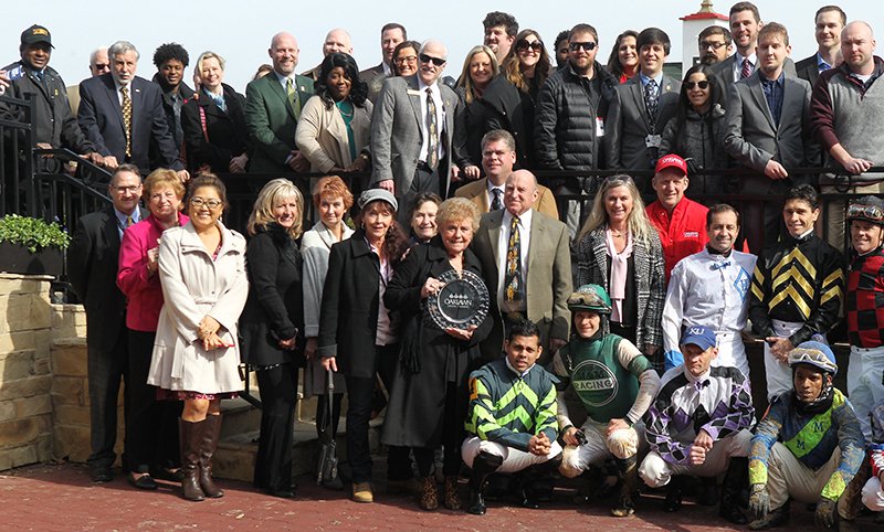 The Sentinel-Record/Richard Rasmussen WINNING CONNECTIONS: Jeannette Snyder, surrounded by her family and friends, as well as Oaklawn Park employees and jockeys, presents the trophy to the winning connections in the Larry Snyder Winner's Circle following the first race Friday at Oaklawn Park. Jeanette Snyder is the wife of legendary jockey and longtime Oaklawn steward Larry Snyder, who died in late October.