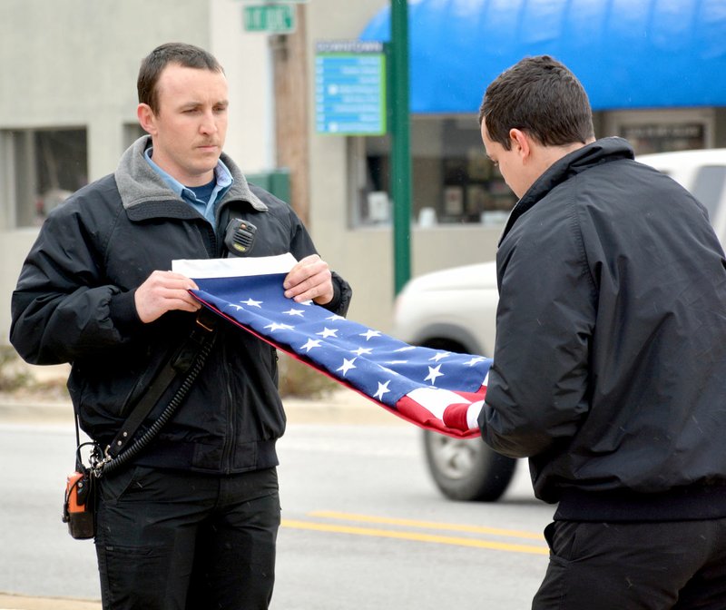 Janelle Jessen/Siloam Sunday Firefighters Justin Bailey, left, and Josh Donahue took down the U.S. Flag that flew in front of Fire Station No. 2 and folded it during a ceremony on Wednesday morning. The flag was be put away for safekeeping and will be returned to its original place when renovations are complete.