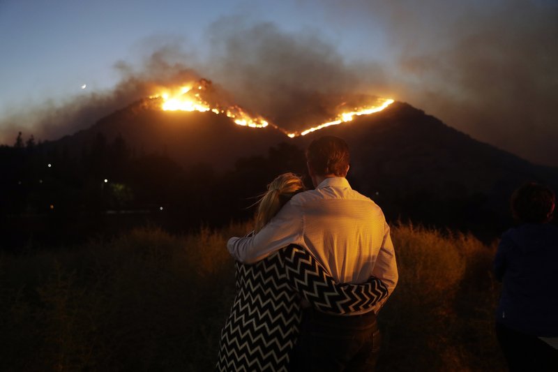 In this Nov. 9, 2018 file photo, Roger Bloxberg, right, and his wife, Anne, embrace as they watch a wildfire on a hill top near their home in West Hills, Calif.  (AP Photo/Marcio Jose Sanchez, File)