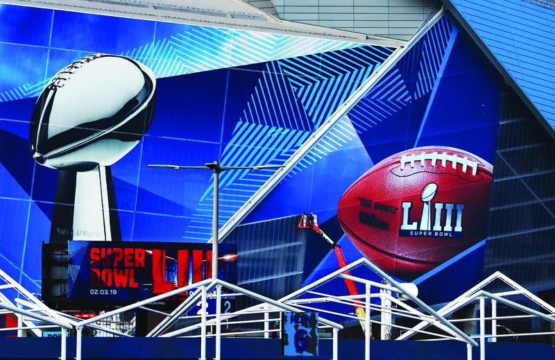 In this  Jan. 17 photo,  workers use a lift to install a Super Bowl 53 wrap on the outside of Mercedes-Benz Stadium as it is transformed for the big NFL football game in Atlanta.   Kraft Heinz’ frozen-food brand Devour is trying to make waves during its Super Bowl debut with an ad taking a humorous jab at one man’s “frozen food porn addiction.” Super Bowl ads have long used raunchiness and sex stand out during the Super Bowl, advertising’s biggest stage. But the approach runs the risk of offending the audience. (Curtis Compton/Atlanta Journal-Constitution via AP, File)