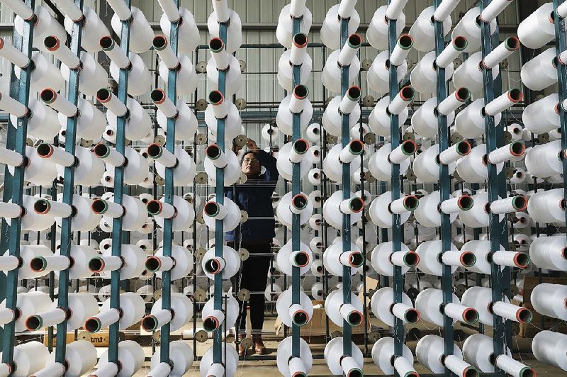 In this January photo, a worker adjusts a cotton string roll at a textile factory in Hangzhou in east China’s Zhejiang province. 