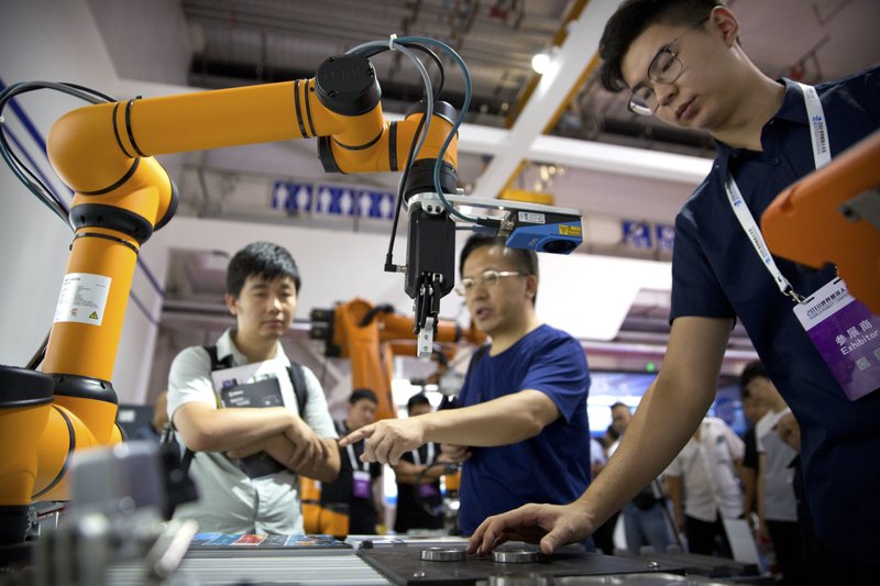 FILE - In this Aug. 18, 2018, file photo, visitors look at a manufacturing robot from Chinese robot maker Aubo Robotics at the World Robot Conference in Beijing, China. China&#x2019;s government has appealed to Washington to accept its industrial progress after U.S. intelligence officials said Beijing helps to steal and copy foreign technologies. (AP Photo/Mark Schiefelbein, File)