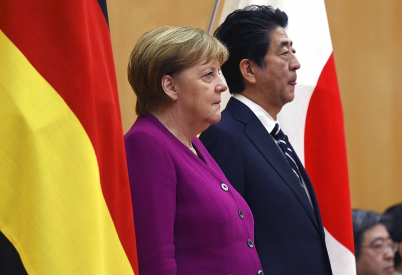 German Chancellor Angela Merkel, left, and Japanese Prime Minister Shinzo Abe, right, stand together as they observe honor guards ahead of a meeting at Abe's official residence in Tokyo Monday, Feb. 4, 2019. (Toshifumi Kitamura/Pool Photo via AP)