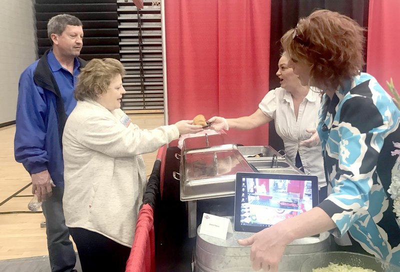 Sally Carroll/McDonald County Press McDonald County neighbors enjoyed food samples at last year's Chamber of Commerce Business Expo at the McDonald County High School. Here, Pineville Elementary kitchen manager Michelle Stites (back, right) gives Sheila Gideon Foreman a chicken sandwich, while Michael Fuller (far, left) and McDonald County High School cafeteria manager Shannon Gravette look on. This year's event is set for Saturday, March 30. The expo gives businesses the opportunity to showcase their services.