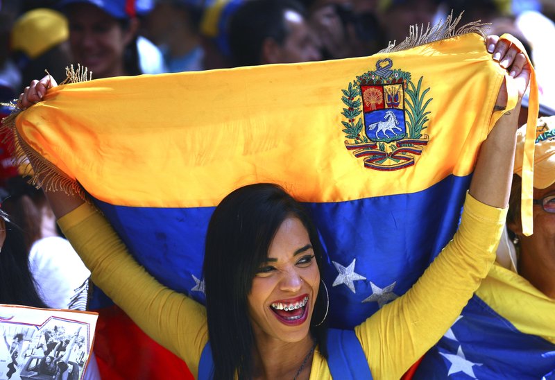A woman, holding a Venezuelan national flag, smiles as she listens to opposition leader and self-proclaimed interim president Juan Guaido during a demonstration against the government of President Nicolas Maduro, in Caracas, Venezuela, Tuesday, Feb. 12, 2019. Venezuela's opposition has called its supporters into the streets across the country in a campaign to break the military's support of Maduro, who refuses to let emergency food and medicine from the United States across the border.(AP Photo/Boris Vergara)