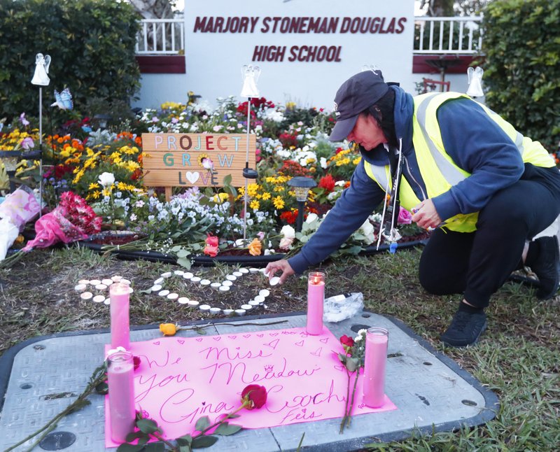 School crossing guard Wendy Behrend lights a candle at a memorial outside Marjory Stoneman Douglas High School during the one-year anniversary of the school shooting, Thursday, Feb. 14, 2019, in Parkland, Fla. A year ago on Thursday, 14 students and three staff members were killed when a gunman opened fire at the high school. (AP Photo/Wilfredo Lee)

