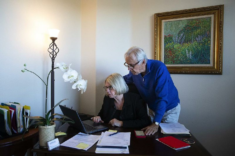 Debbie Douglas works on her computer as her husband and business partner, Gary, stands by in their home office in Newport Beach, Calif.