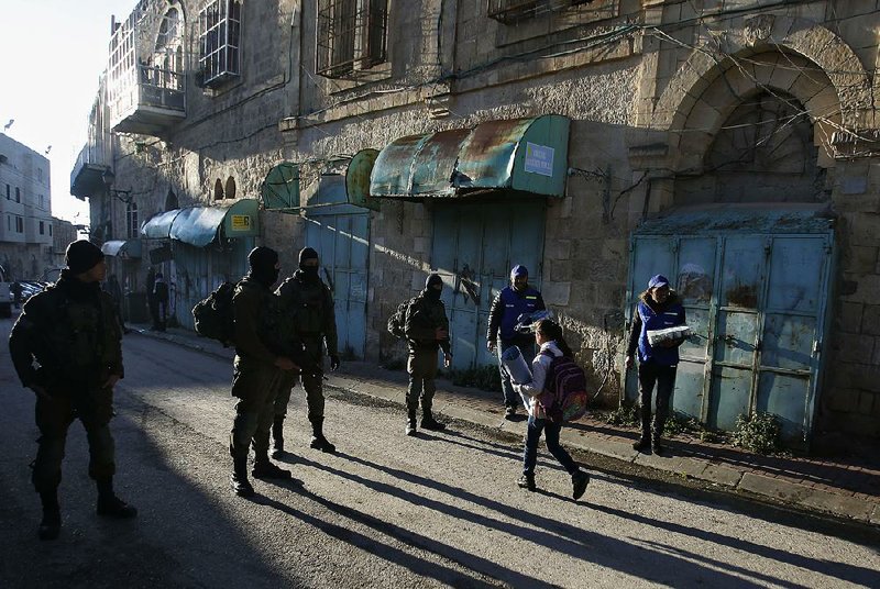 Palestinian observers (right) keep an eye on children walking past Israeli soldiers Tuesday on their way to school in the West Bank city of Hebron. Palestinian activists are handling patrols to document alleged Israeli settler violence. 