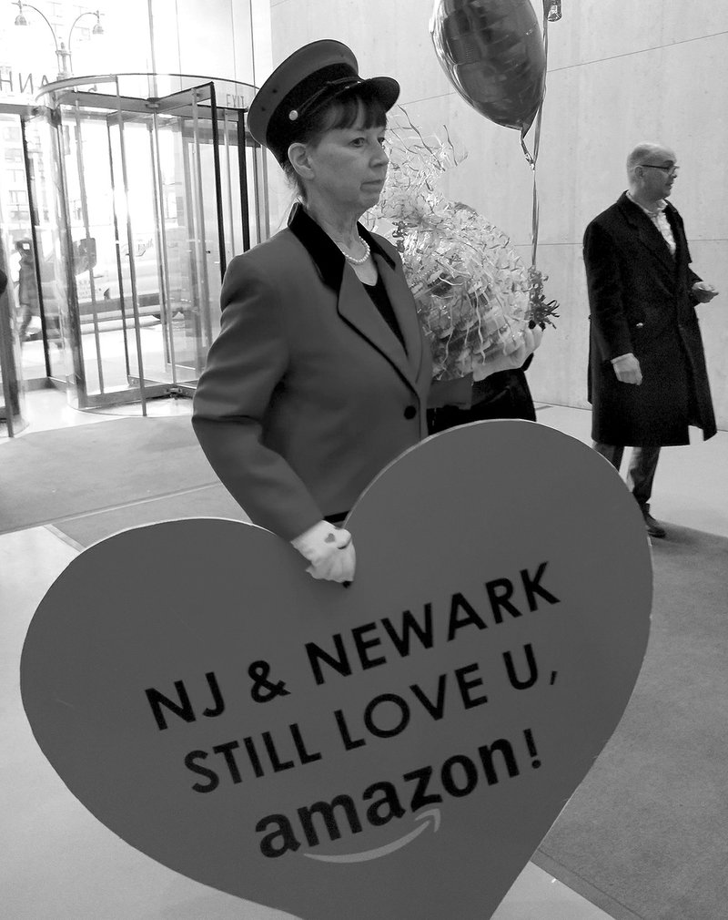 The Associated Press NEW SITE: In this Thursday photo provided by Newark Alliance, Laurie Ross, an actor with the event planners at Life 'O the Party, holds a message reading "NJ &amp; Newark Still Love U, Amazon!" while arriving at an Amazon office in New York. The love note came despite Amazon saying it's not seeking a new site.