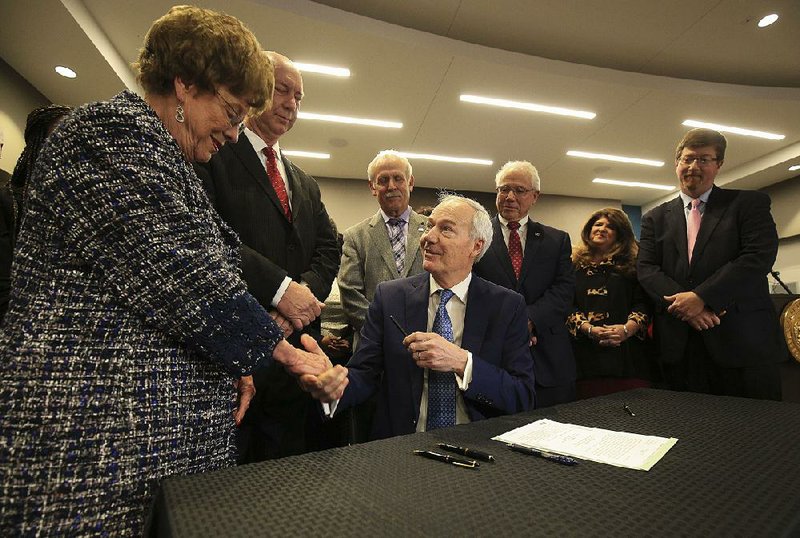 Gov. Asa Hutchinson hands a pen used to sign HB1145 into law Monday to Sen. Jane English (left), R-North Little Rock, one of the primary sponsors of the bill along with Rep. Bruce Cozart (second from left), R-Hot Springs, at the Department of Education in Little Rock. The law raises teacher salaries starting in July. 