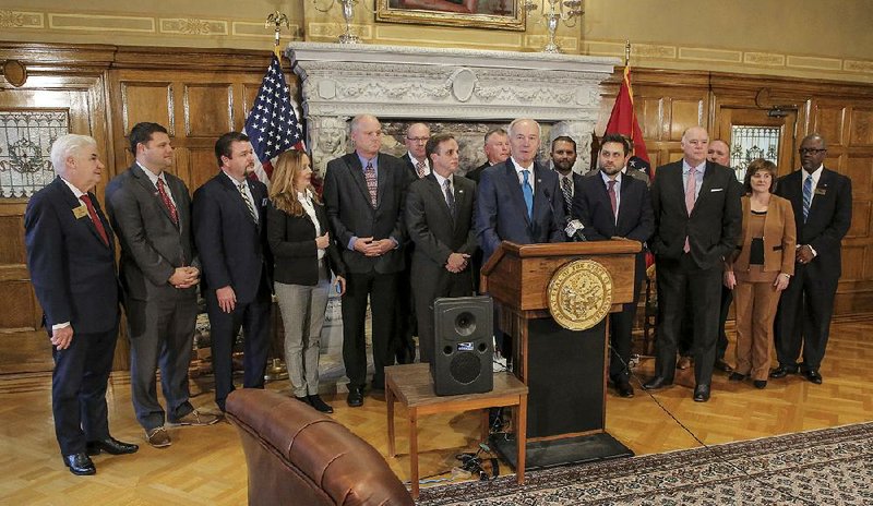 Gov. Asa Hutchinson (at lectern) stands with lawmakers Tuesday at the state Capitol after signing a bill to cut the state’s top income-tax rate. 