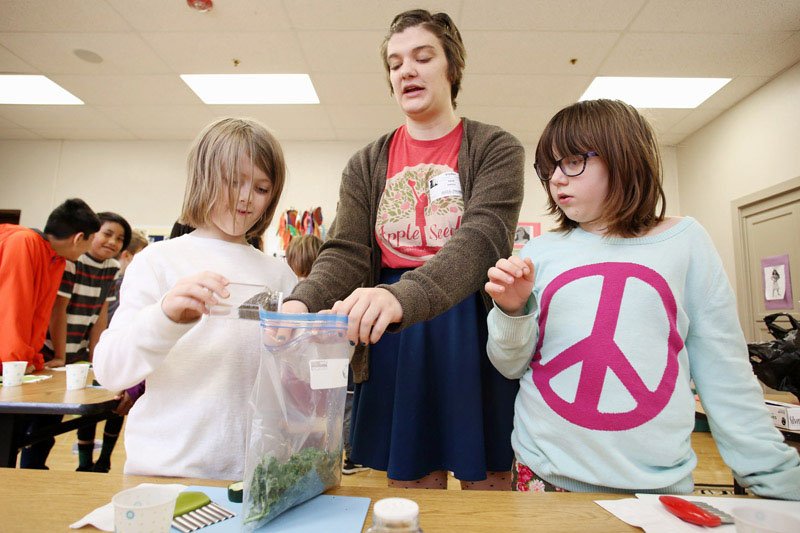 NWA Democrat-Gazette/DAVID GOTTSCHALK Erin Hayes (center), cooking in schools coordinator with Apple Seeds NWA, helps Thursday, February 21, 2019, Pax Carroll (left) and Anastasia Collins, both third grade students at Washington Elementary School, mix seasonings with kale at the school in Fayetteville. Apple Seeds visited three classes at the school and instructed the students on how to make kale and cucumber chips and review nutritional information available on the labeling of food products.
