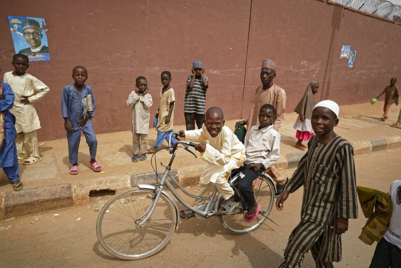 Young boys leave on a bicycle after making traditional Muslim Friday prayers, past a campaign poster for President Muhammadu Buhari, left, outside the central mosque in his hometown of Daura, in northern Nigeria Friday, Feb. 22, 2019. Nigerians are preparing to go to the polls for a presidential election Saturday, one week after a surprise delay for Africa's largest democracy. (AP Photo/Ben Curtis)