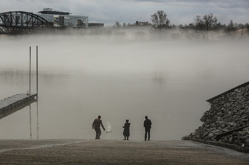 Cameron Franklin (from left) and his siblings Sydney Johnson, 10, and Zachary Johnson, 13, all of North Little Rock, skip stones from the dock at Riverfront Park as a fog rolls in Saturday in North Little Rock. During the day Saturday, parts of the state were under severe weather watches, flood warnings and watches, and fog and wind advisories.