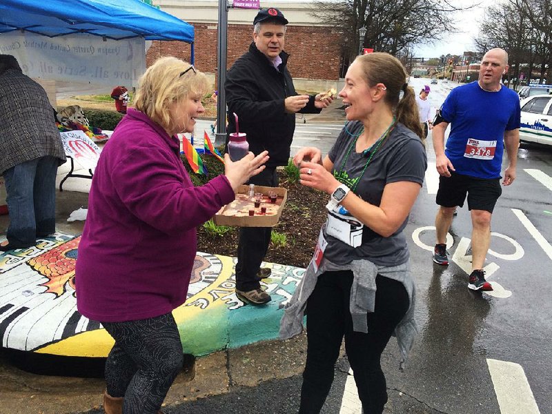 The Rev. Anne Holcomb (left), a retired pastor and member of Quapaw Quarter United Methodist Church in Little Rock, gives Communion in the form of tiny cups of grape juice during the 2018 Little Rock Marathon along with the Rev. Keith Coker, Quapaw Quarter’s pastor (center). The church will offer “Communion on the Run” for all who wish to partake on Sunday from 8-10 a.m. at the intersection of 16th and Main streets in Little Rock during this year’s marathon, according to Holcomb.