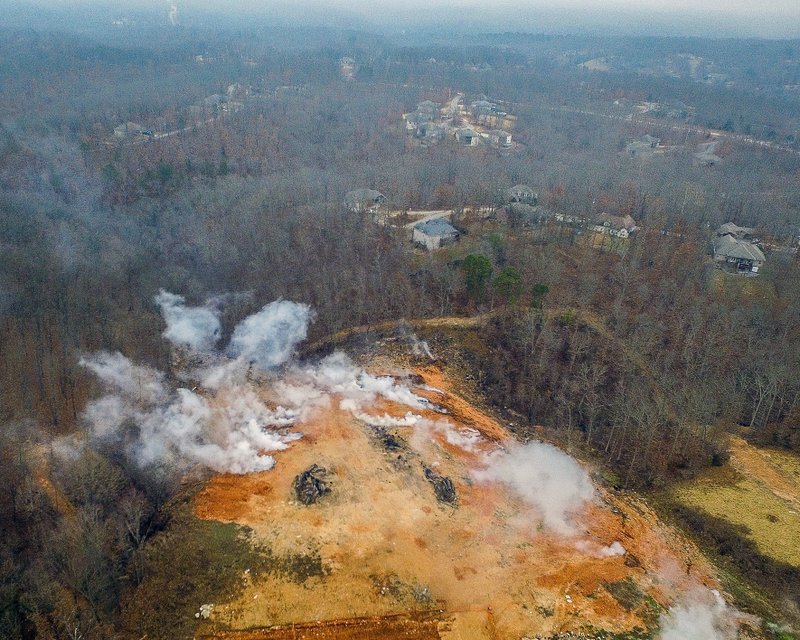 In this Friday, March 1, 2019 photo provided by Apex Visual Solutions smoke rises from an underground fire at an illegal dumping site in Bella Vista, Ark. The fire, which started in July, is beneath dozens of feet of waste and dirt in a former dump intended for tree limbs and stumps. It has been smoldering for at least seven months, sending noxious smoke throughout the community, with costs to extinguish it estimated in the tens of millions. (C. Nelson/Apex Visual Solutions via AP)