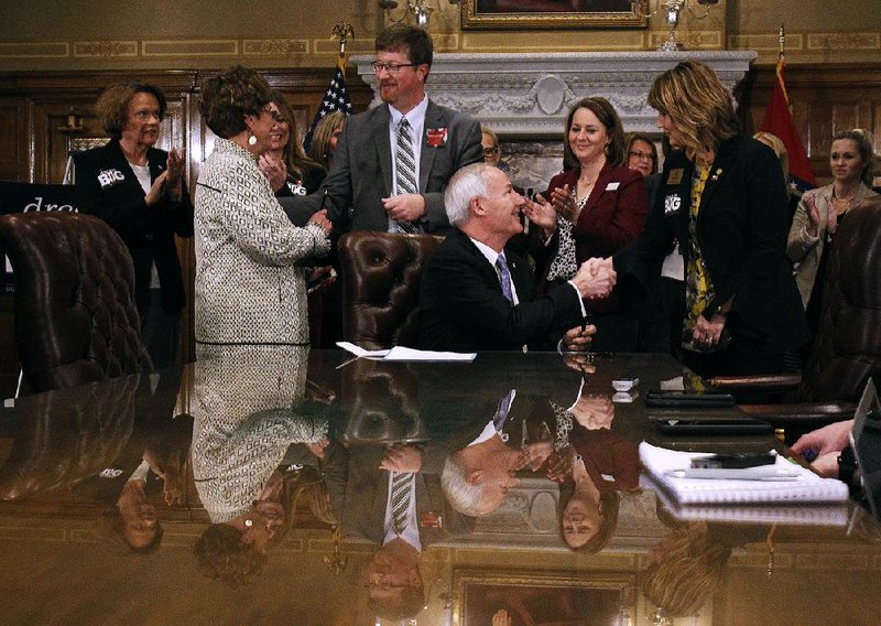 Gov. Asa Hutchinson (seated) shakes hand Wednesday with Rep. Sonia Eubanks Barker, R-Smackover, after signing Senate Bill 153, part of the “Dream Big for Arkansas” initiative by the Republican Women’s Legislative Caucus. The bills address education, juvenile justice, economic development, day care and health care. In the morning, Hutchinson also signed a bill to convert a former prison facility into a place to help veterans re-enter society. More photos available at www.arkansasonline.com/arkansasonline.com/306genassembly