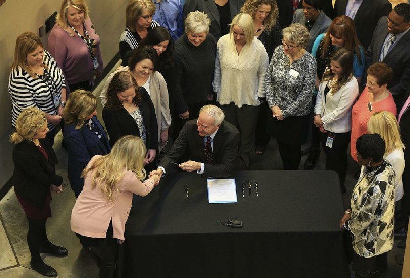 Gov. Asa Hutchinson hands a pen to Sen. Breanne Davis after signing the bill on school counselors on Thursday. A group of educators and school counselors was on hand to see the bill become law. 