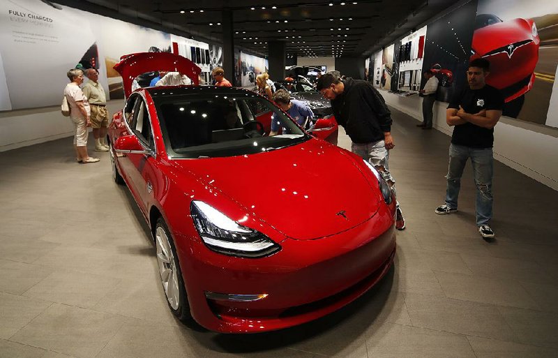 Customers talk to a Tesla salesman as a Model 3 sits on display last summer in a showroom in Denver. Just days after announcing that it would close most of its stores, Tesla said Monday it will keep “significantly more stores open” than previously announced. 