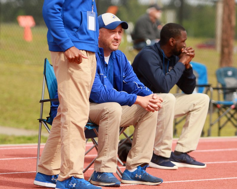 SAU track coach Tim Servis (seated left) watches the action during last season’s GAC Championships at the Mulerider Track Complex. This year’s championships will be held at Oklahoma Baptist on April 18-20.