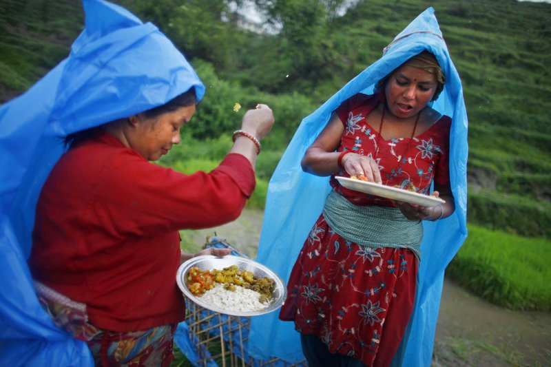 In this June 30, 2014, file photo, a farmer, left, ritualistically offers a small portion of food to God before eating her lunch while working at a rice field in Chunnikhel, Katmandu, Nepal. (AP file photo/Niranjan Shrestha)