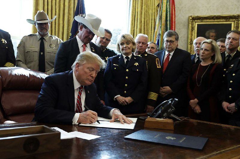 President Donald Trump signs the first veto of his presidency Friday in the Oval Office as Attorney General William Barr (right) and law enforcement officials look on. The veto overruled Congress’ rejection of his emergency declaration for border wall funding. 