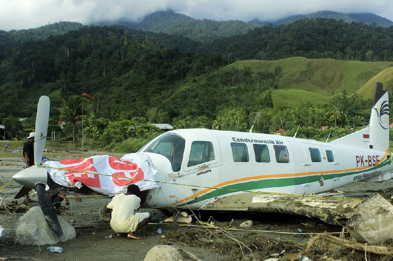 A man examines a plane Sunday in Sentani, Indonesia, at the place where the aircraft came to rest after being washed away during a flash flood. 