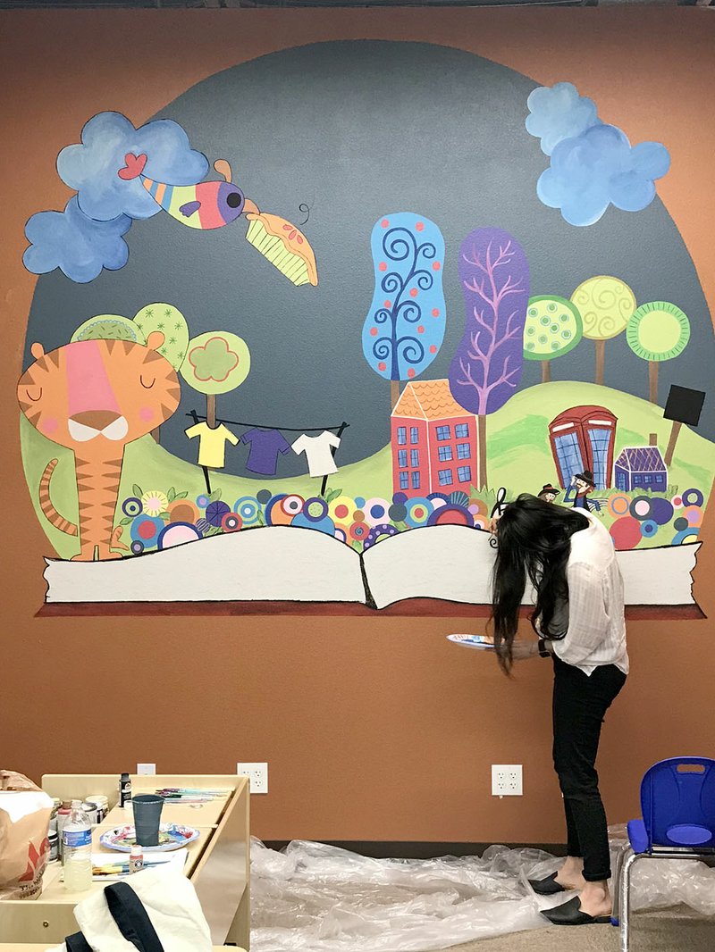 Courtesy Photo Laura Hicky Kraus of Prairie Grove works on a mural in the children's section at the new Prairie Grove Public Library. It shows features of the community coming out of an open book, including the Clothesline Fair, downtown, hills in the background, square dancing and the Prairie Grove Tigers.