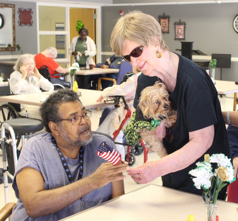 Thank you: Pat Qualls, right, hands a small American flag to U.S. Army veteran John Gaines, left, at Courtyard Health & Rehabilitation on Monday. Qualls is holding her dog, Sadie, who accompanies Qualls almost everywhere. Qualls works with the local VFW to organize monthly events honoring veterans at local nursing homes.